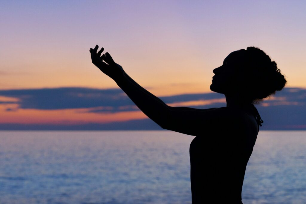 woman with arms outstretched toward the setting sun while meditating